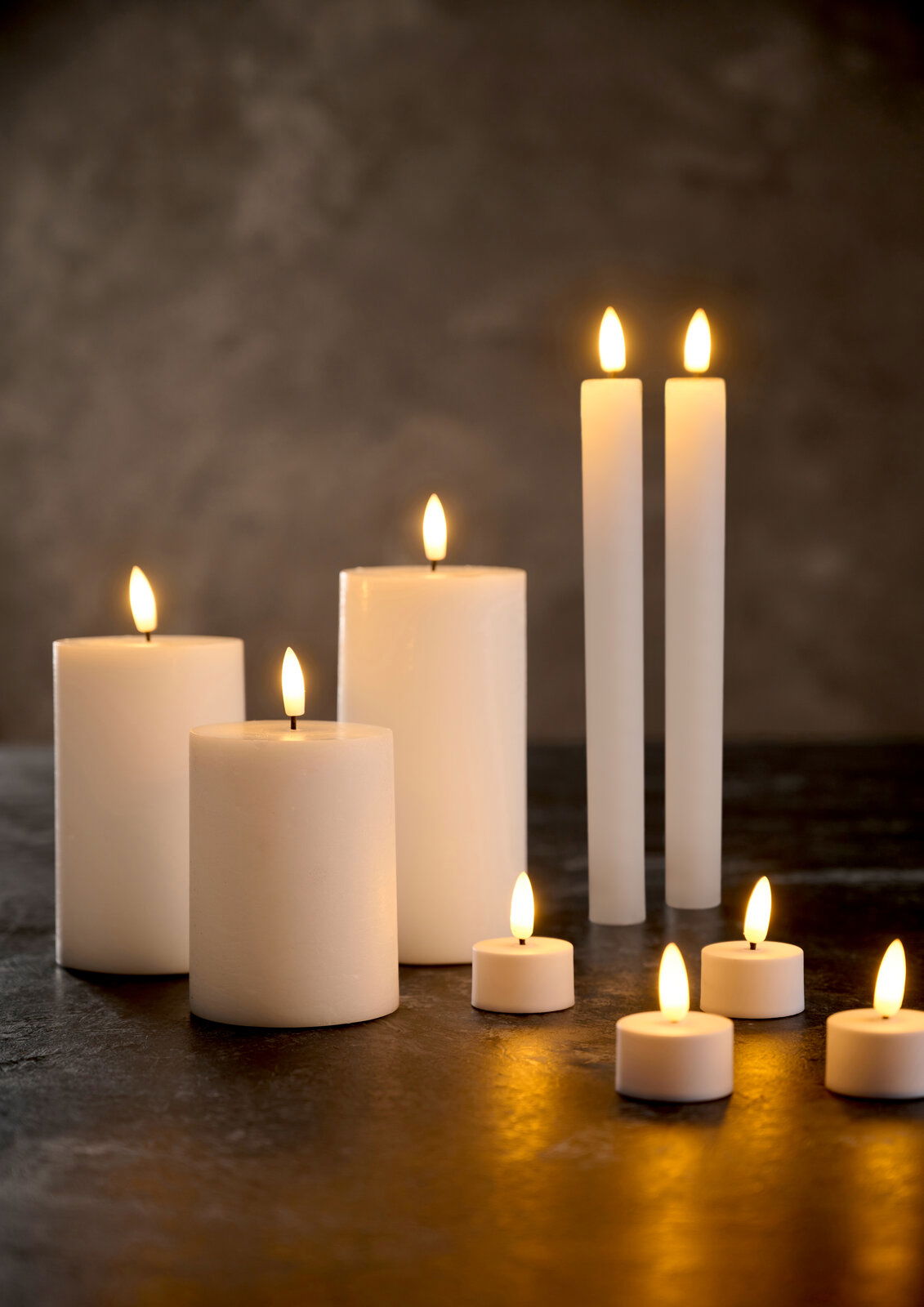 Verschiedene LED-Kerzen in unterschiedlichen Größen und Formen, die auf einem dunklen Untergrund leuchten. Die Perspektive zeigt die Kerzen von vorne.