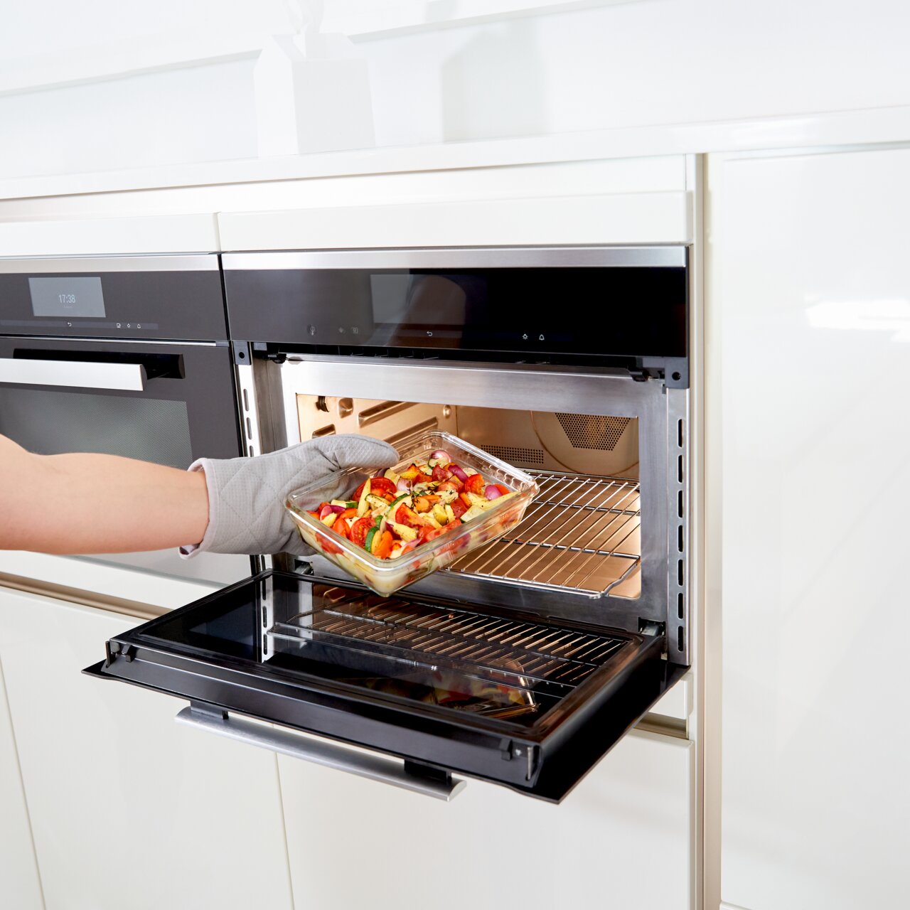 Rechteckige Glasform mit 1,30 L Fassungsvermögen, gefüllt mit Gemüse, wird aus einem modernen Backofen entnommen. Seitliche Perspektive.