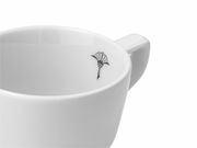 Nahaufnahme einer weißen Espressotasse mit einem schwarzen Logo auf der Innenseite, seitliche Perspektive.