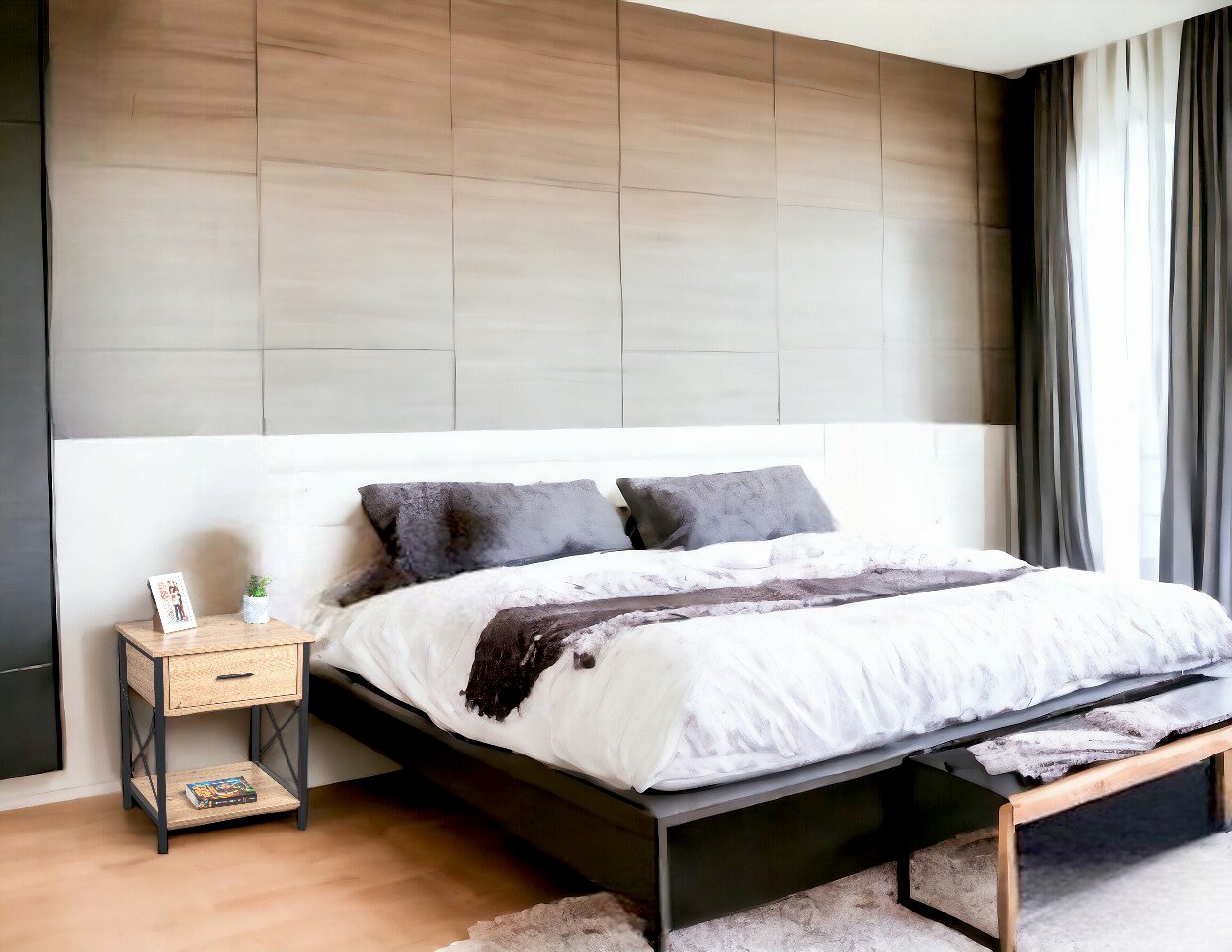 Modernes Schlafzimmer mit großem Doppelbett in weiß-grauer Bettwäsche, Nachttisch im Holz-Metall-Design und gepolsterter Wandverkleidung Perspektive: schräg von vorne rechts aufgenommen.