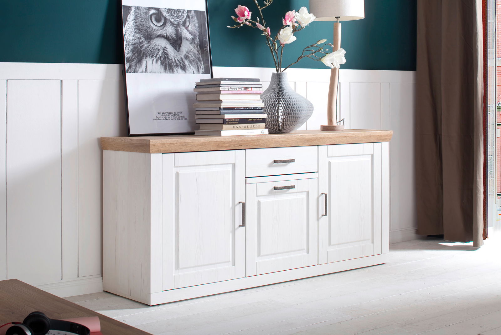 Weißes Sideboard mit Holzplatte, dekoriert mit Büchern, Vase und Lampe, seitliche Perspektive