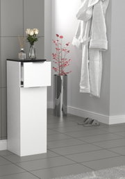 Weißer, schlanker Badezimmer-Hochschrank mit schwarzer Ablage und geöffneter Schublade, frontale leicht seitliche Perspektive; daneben glänzender zylindrischer Pflanzkübel im modernen Badambiente.