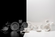 Schwarz-weißes Disney-Tischgeschirr-Set mit Mickey- und Minnie-Motiven (Teller, Tassen, Schalen) neben Geschenkboxen mit Schleifen, frontal in leicht erhöhter Perspektive auf zweifarbigem Studiohintergrund präsentiert.