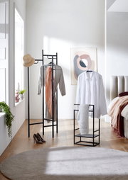 Heller Schlafbereich mit schwarzem Metall-Kleiderständer und passendem Kleiderstuhl, behängt mit Hemd, Kleid, Schal und Hut; Frontansicht auf die Garderobenmöbel im Raum