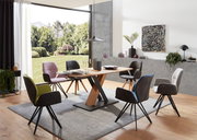 Moderner Essbereich mit einem Esstisch aus Holz und schwarzen Metallbeinen, umgeben von verschiedenen Armlehnstühlen in unterschiedlichen Farben. Die Perspektive zeigt den Raum von der Seite mit Blick auf den Tisch und die Stühle, im Hintergrund ist ein g