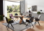 Moderner Essbereich mit einem Esstisch aus Holz und schwarzen Metallbeinen, umgeben von verschiedenen Armlehnstühlen in unterschiedlichen Farben. Die Perspektive zeigt den Raum von der Seite mit Blick auf den Tisch und die Stühle, im Hintergrund ist ein g