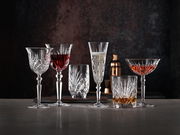 Verschiedene Kristallgläser mit Getränken, frontal auf einem Tisch vor dunklem Hintergrund arrangiert.