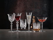 Verschiedene Kristallgläser mit Getränken, frontal auf einem Tisch vor dunklem Hintergrund arrangiert.