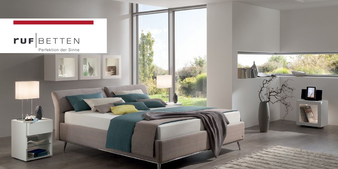 Ein modernes Schlafzimmer mit großem Bett, stilvollen Möbeln und viel Tageslicht durch große Fenster.