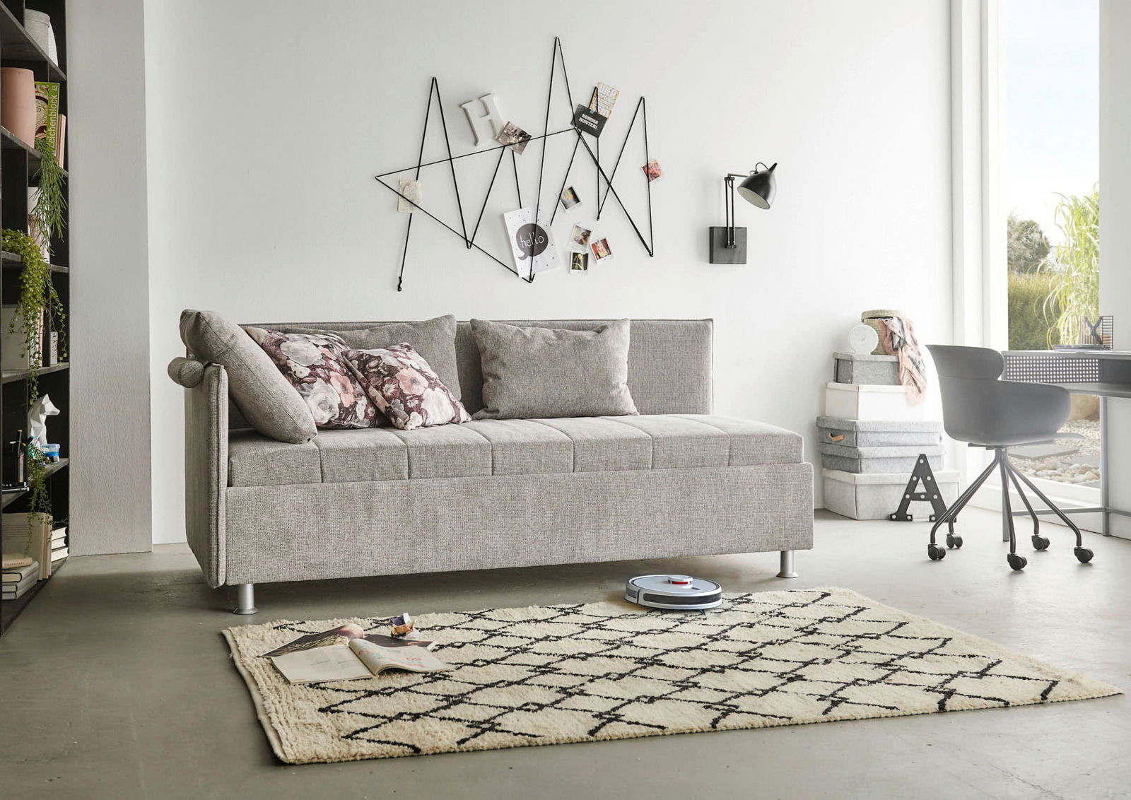 Graue Polsterliege in modernem Wohnzimmer, seitliche Perspektive, mit dekorativen Kissen und geometrischer Wanddekoration.