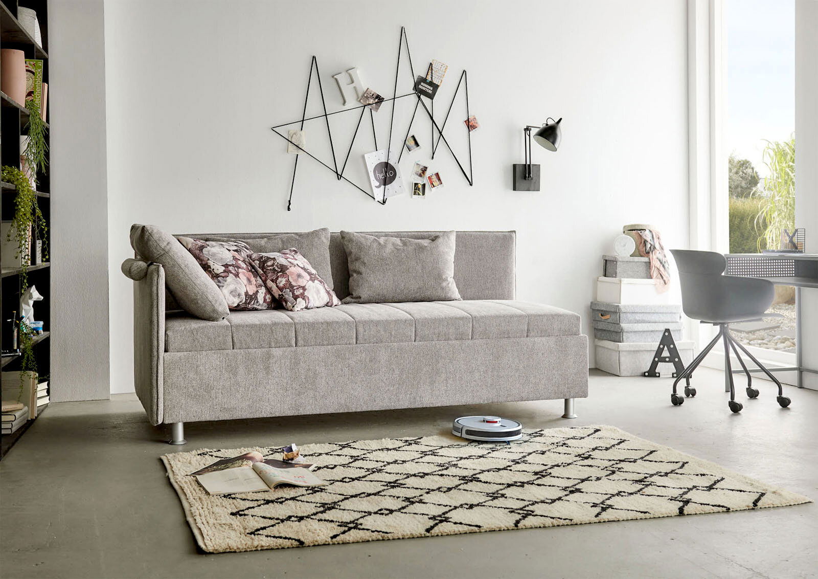 Beldomo Sleep Polsterliege ohne Umbau SANDRO Graue Polsterliege in modernem Wohnzimmer, seitliche Perspektive, mit dekorativen Kissen und geometrischer Wanddekoration.