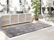 Moderner Designer Teppich in Grau- und Rottönen, in einem hellen Wohnzimmer mit Blick auf ein Sideboard und Pflanzen.