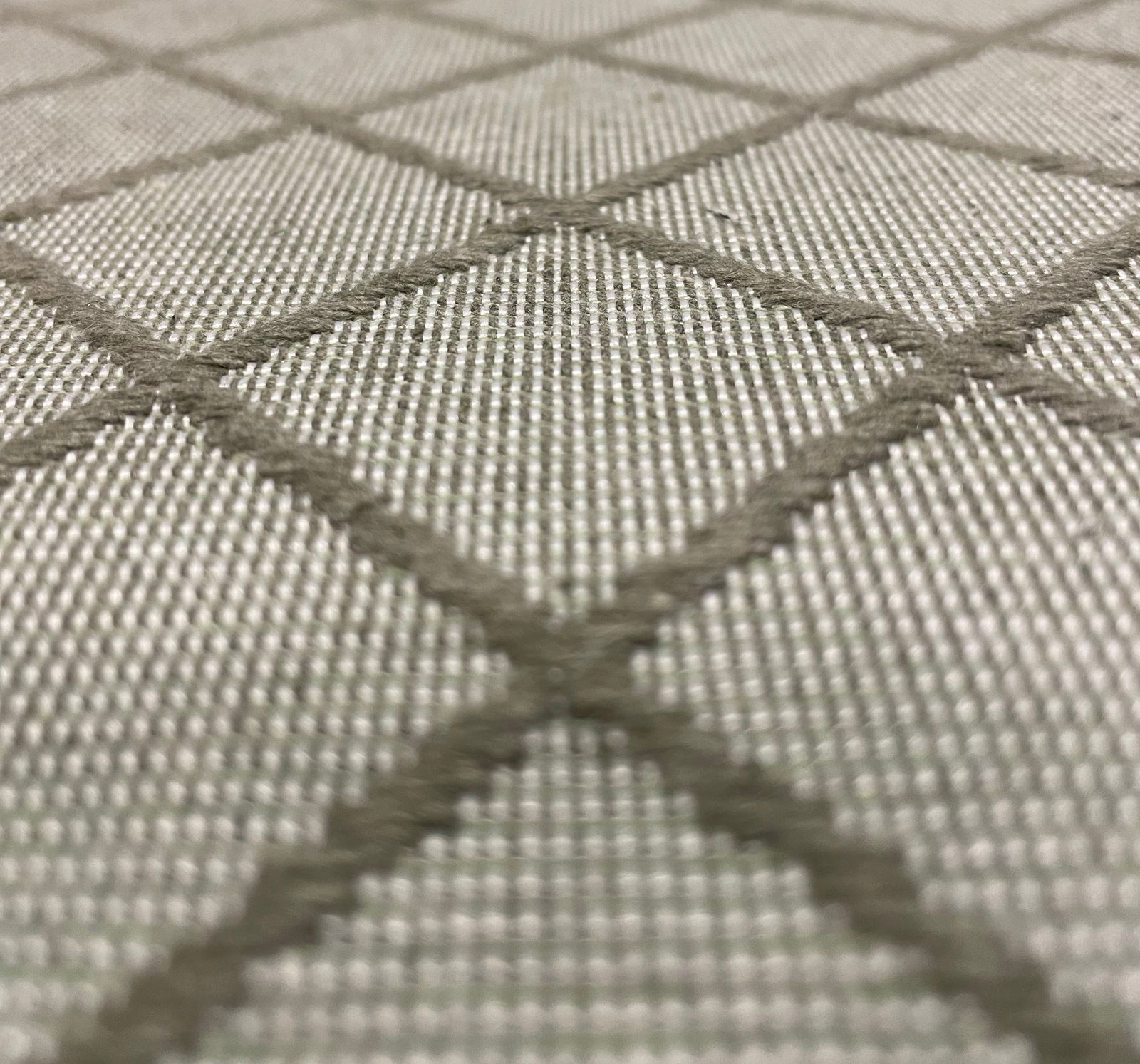 Nahaufnahme einer Mittellehnerauflage mit grauem Rautenmuster aus texturiertem Stoff, perspektivisch von der Seite aufgenommen.