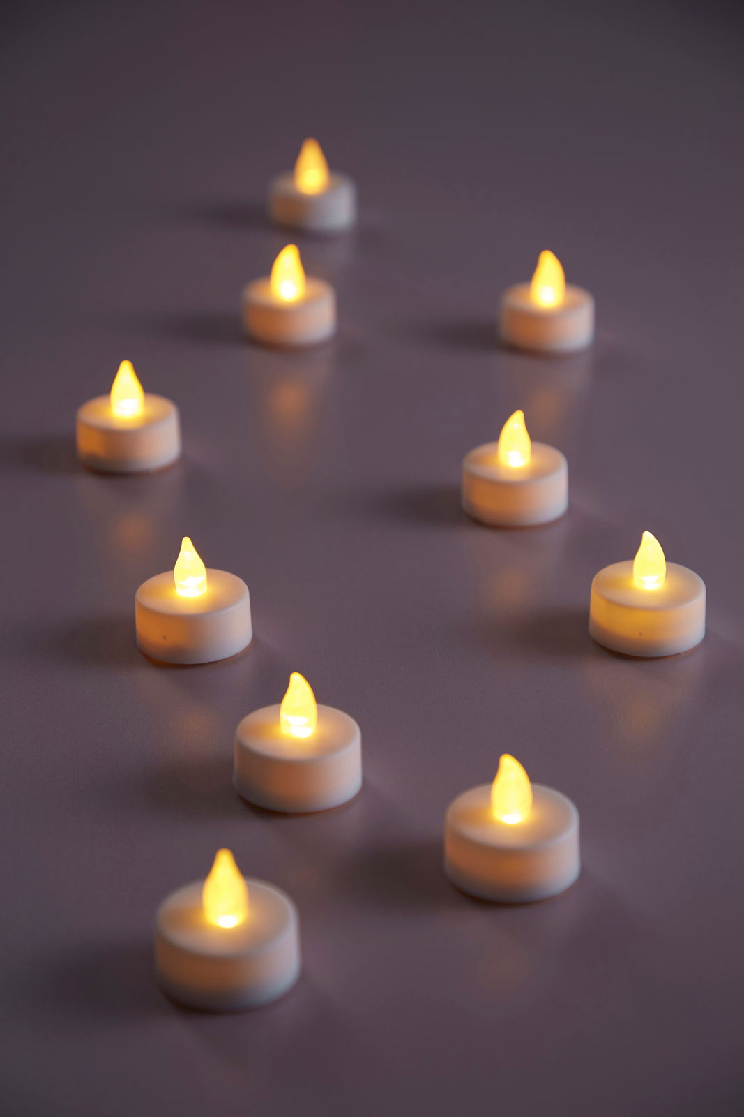 Mehrere LED-Teelichter in warmem Gelbton auf einer Oberfläche, aus seitlicher Perspektive fotografiert.