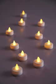 Mehrere LED-Teelichter in warmem Gelbton auf einer Oberfläche, aus seitlicher Perspektive fotografiert.