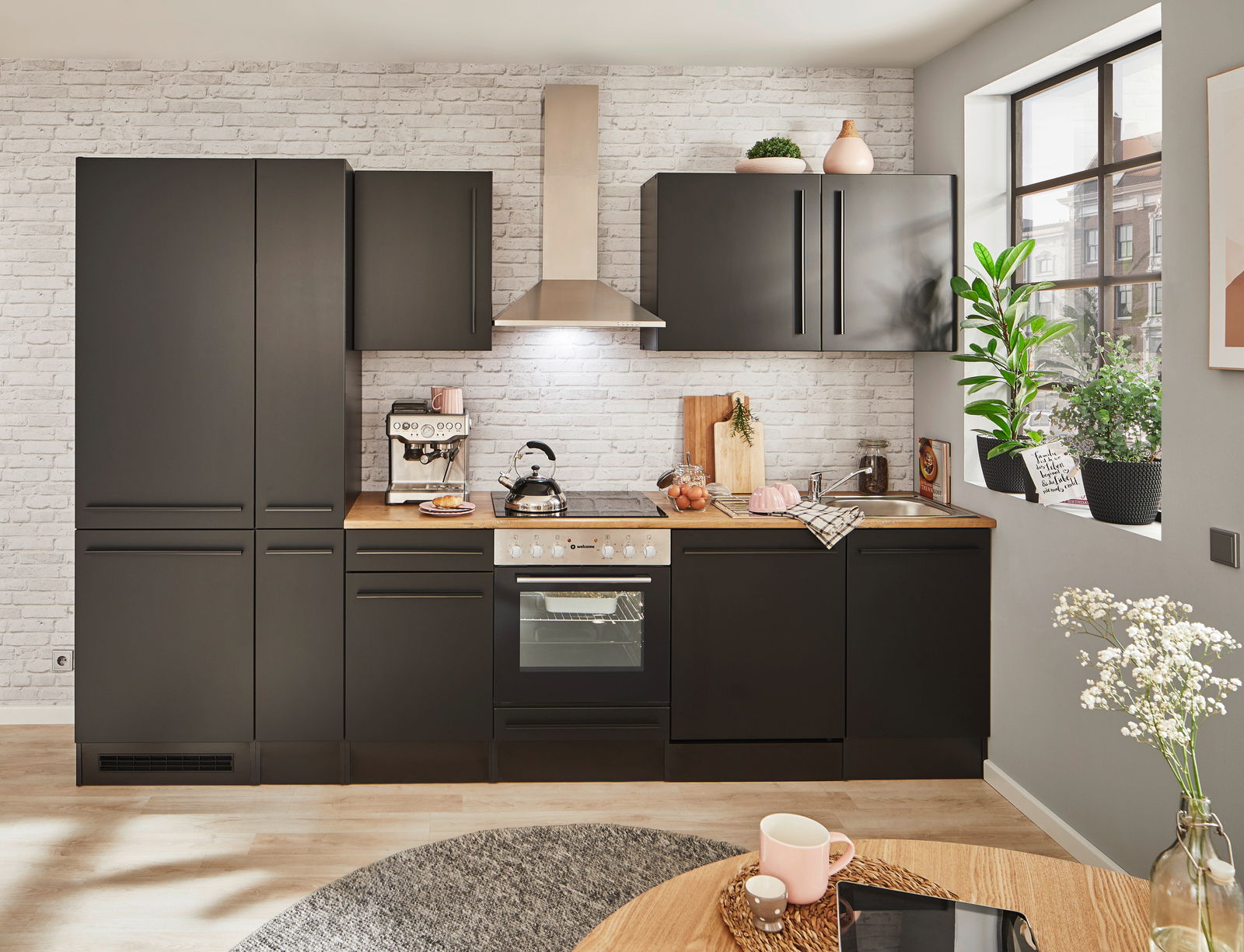 Moderne schwarze Küchenzeile mit Backofen, Herd und Dunstabzugshaube, umgeben von weißen Backsteinwänden, aus der Perspektive eines Esszimmers mit Blick auf die Küche.