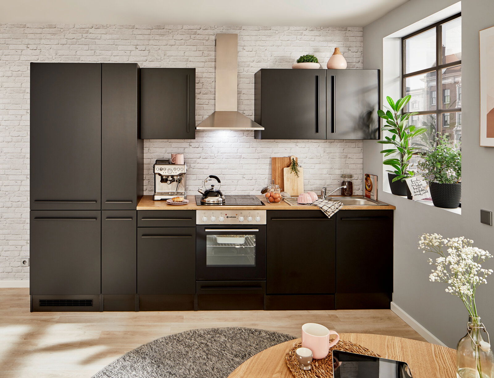 Moderne schwarze Küchenzeile mit Backofen, Herd und Dunstabzugshaube, umgeben von weißen Backsteinwänden, aus der Perspektive eines Esszimmers mit Blick auf die Küche.