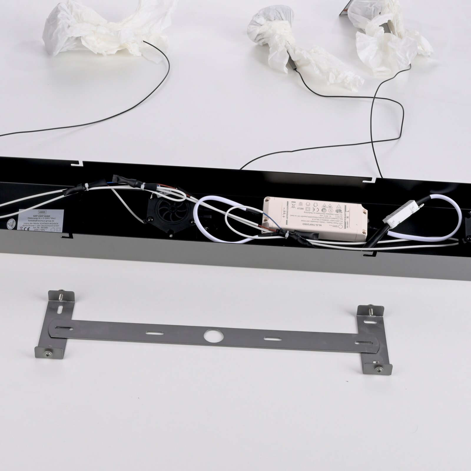 Innenansicht einer schwarzen LED-Leuchte mit sichtbar verlegter Verkabelung, Netzteil und Lüfter sowie separater Metall-Montagehalterung auf weißem Hintergrund, fotografiert aus leicht erhöhter Draufsicht.
