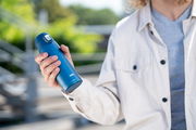 Person hält einen blauen Thermobecher in der Hand, seitliche Perspektive