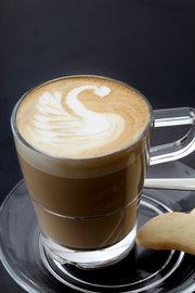 Glas mit Latte Macchiato und Schwan-Latte-Art auf einer Untertasse Senso, seitliche Perspektive