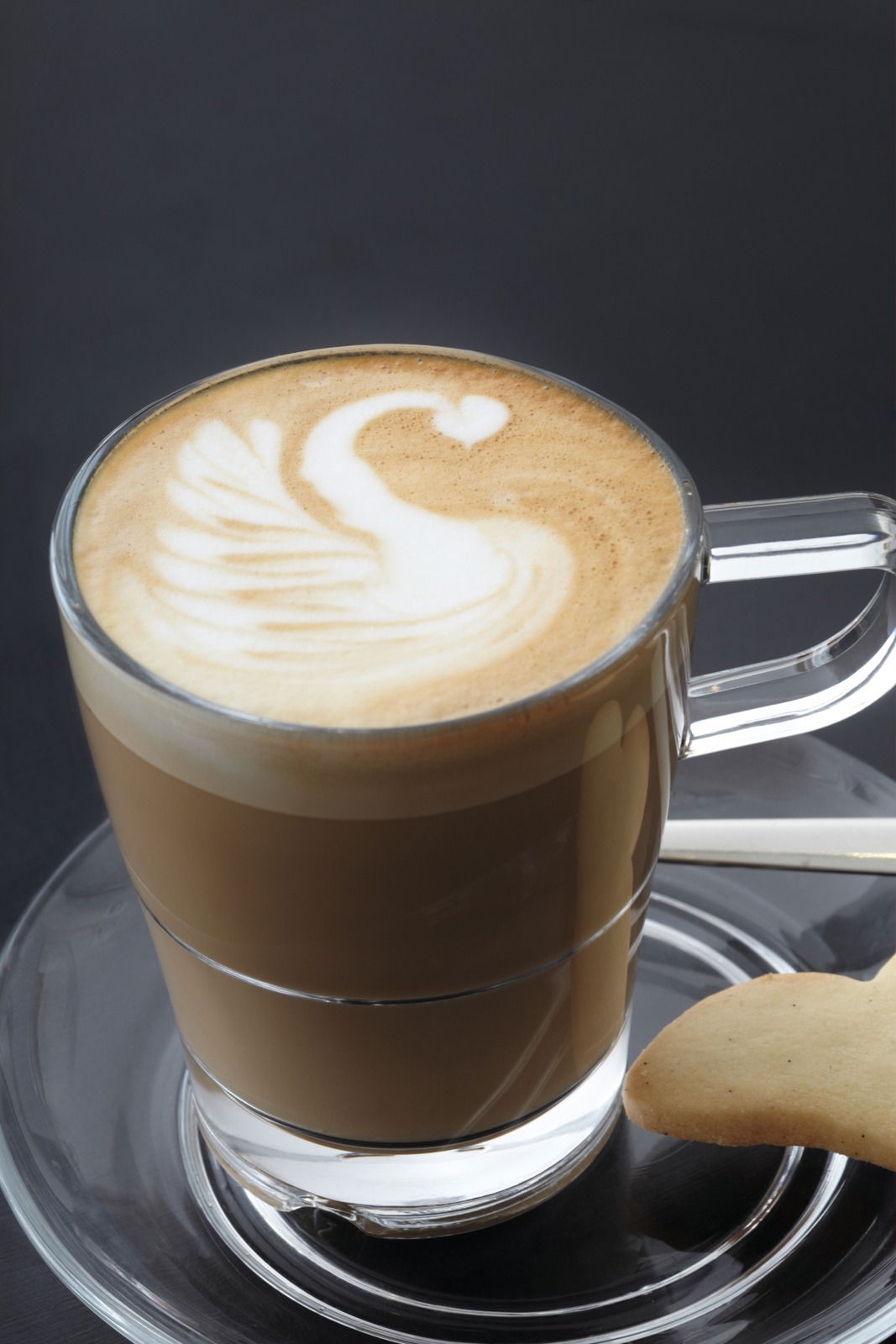 Glas mit Latte Macchiato und Schwan-Latte-Art auf einer Untertasse Senso, seitliche Perspektive