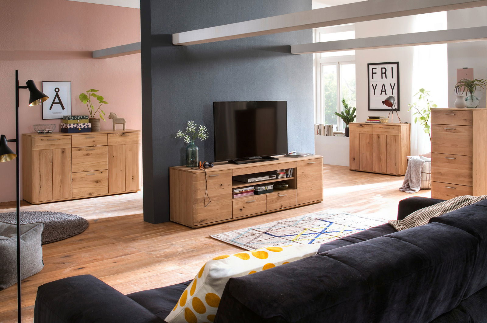 Wohnzimmer mit modernem XL-TV-Lowboard aus Holz, frontal betrachtet, mit Dekorationen und einem großen Fernseher darauf.