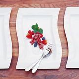 Rechteckiger, weißer Teller mit geschwungenen Kanten, von oben fotografiert, dekoriert mit frischen Beeren und Besteck.