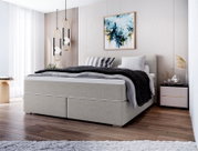 Modernes graues Boxspringbett mit gepolstertem Kopfteil und Bettwäsche in Grau/Schwarz im hellen Schlafzimmer, perspektivisch schräg von vorne links aufgenommen