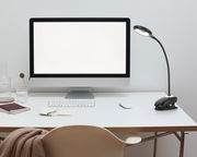 LED-Klemmleuchte auf einem Schreibtisch neben einem Computerbildschirm, seitliche Perspektive