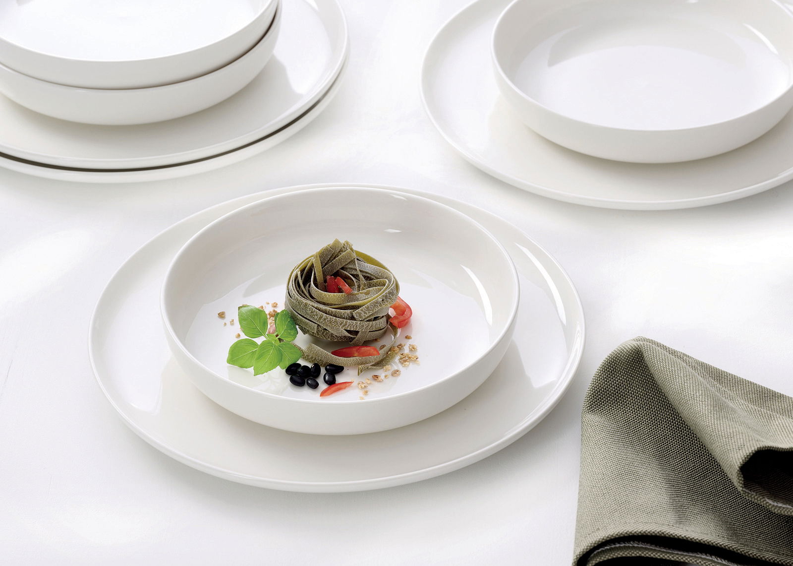 Elegantes Gourmet-Set mit weißen Tellern und Schalen, präsentiert mit einer stilvollen Pasta-Garnitur, aus der Vogelperspektive fotografiert.