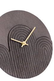 Close-up van een moderne, ronde wandklok met een gestructureerde, donkere wijzerplaat en gouden wijzers, gezien van bovenaf.