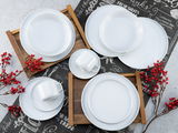 Vogelperspektive auf ein elegantes, weißes Kombiservice-Set mit Tellern, Tassen und Untertassen, dekoriert mit roten Beeren und Holztabletts.