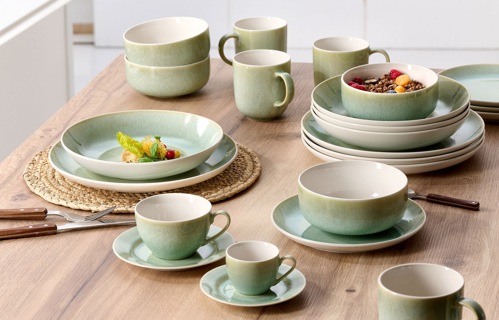 Grünes Tafelset 8-tlg. aus Keramik, bestehend aus Tellern, Schalen und Tassen, auf einem Holztisch von oben fotografiert.