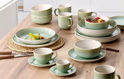 Grünes Tafelset 8-tlg. aus Keramik, bestehend aus Tellern, Schalen und Tassen, auf einem Holztisch von oben fotografiert.