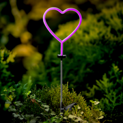 Herzförmige Solar Stabbeleuchtung in lila, aufrecht in einem Garten platziert, umgeben von grünen Pflanzen.