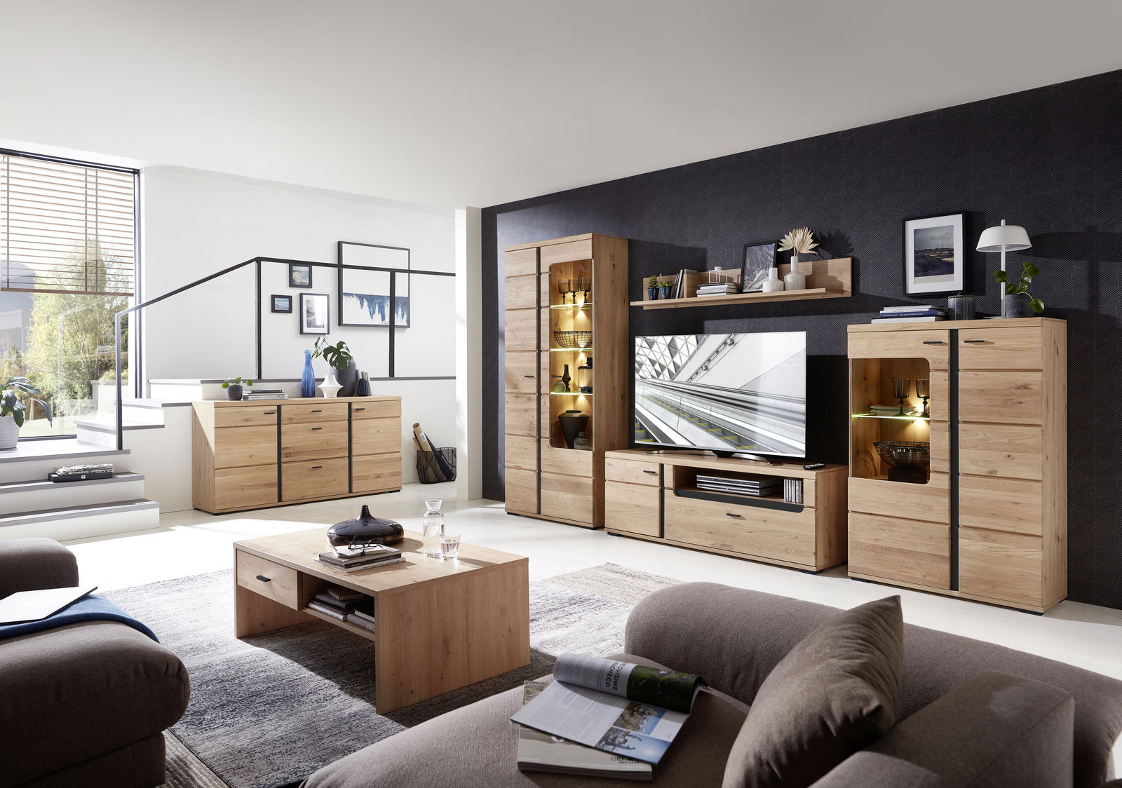 Moderne Wohnzimmermöbel aus Holz, bestehend aus Wohnwand, Sideboard, Vitrine und Couchtisch, in einem hellen Raum mit großen Fenstern, seitliche Perspektive.