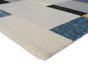 Nahaufnahme eines Frisé-Teppichs mit geometrischem Muster in Blau-, Grau- und Beigetönen, perspektivisch von der Seite aufgenommen.