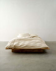 Minimalistisches Bett mit beiger Bettwäsche in Frontalansicht auf einem Holzrahmen.