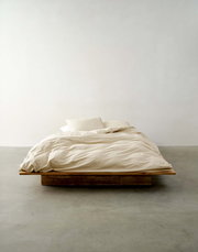 Minimalistisches Bett mit beiger Bettwäsche in Frontalansicht auf einem Holzrahmen.