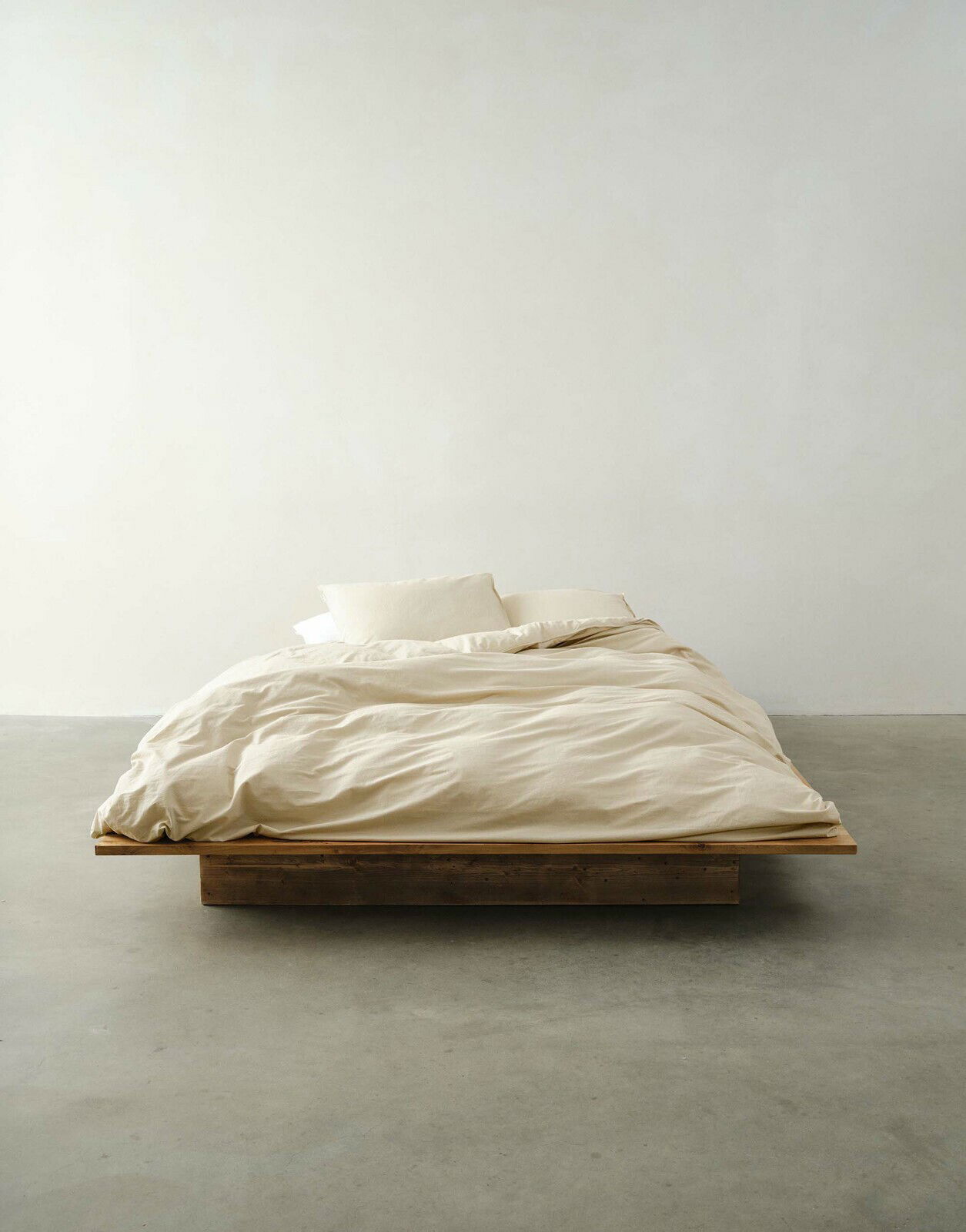 Minimalistisches Bett mit beiger Bettwäsche in Frontalansicht auf einem Holzrahmen.