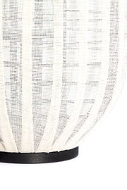 Detailopname vanuit zijaanzicht van een crèmekleurige lamp met geplooid opengeweven textiel en een ronde zwarte voet