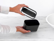 Schwarzer Abfallbehälter mit abnehmbarem Deckel, von oben betrachtet, auf einer Marmoroberfläche.