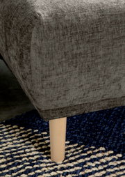 Nahaufnahme einer grauen Rundecke mit Holzbein auf einem blau-weißen Teppich, seitliche Perspektive