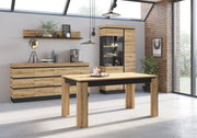 Moderne eethoek met een houten eettafel en zwarte accenten, een dressoir en een vitrinekast op de achtergrond, gezien vanuit de zijkant.