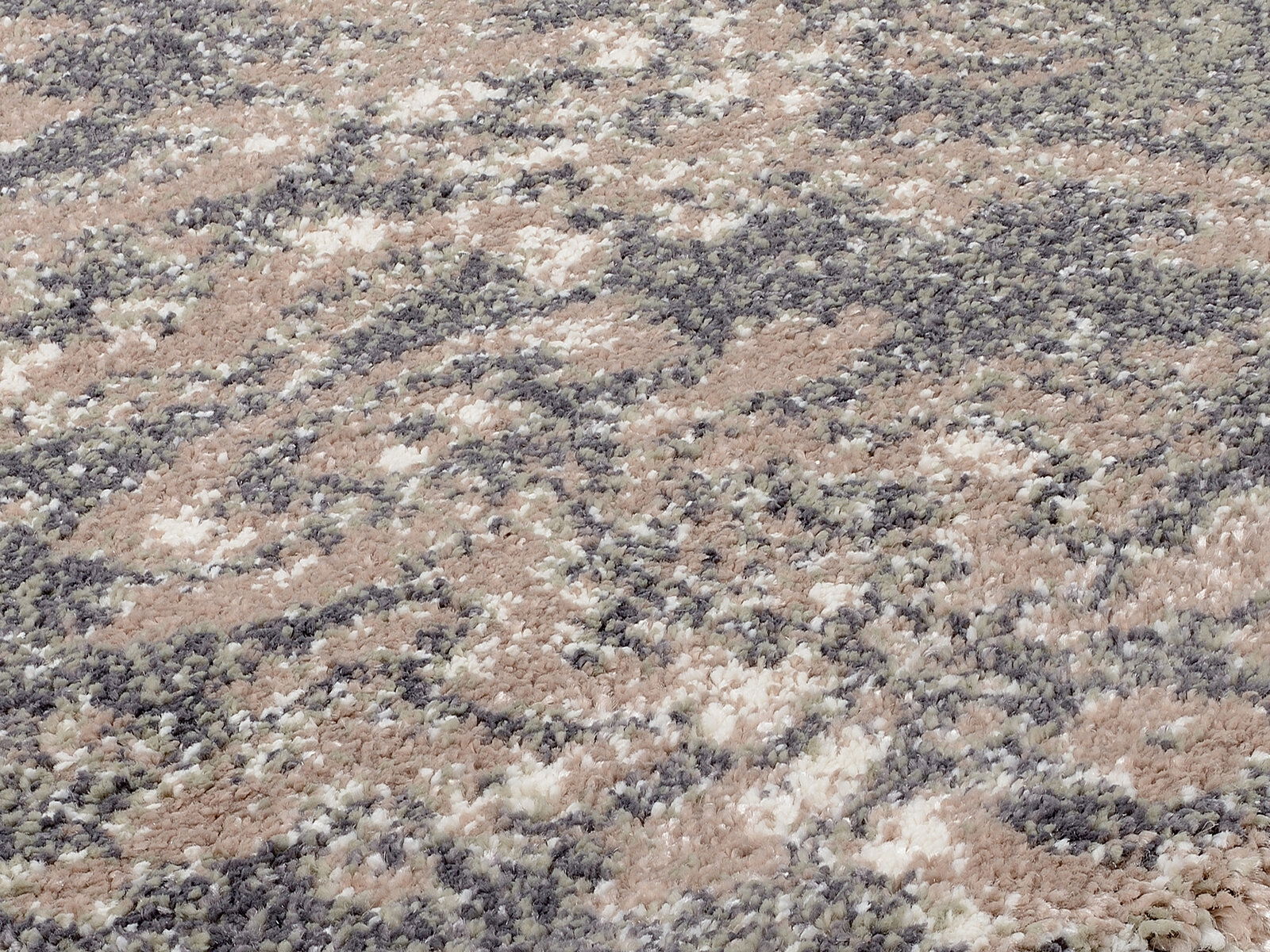 Nahaufnahme eines Designer Teppichs mit gemustertem, mehrfarbigem Flor in Beige-, Grau- und Grüntönen, aus schräger Perspektive aufgenommen.