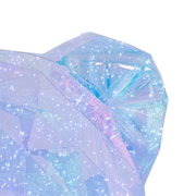 Nahaufnahme eines transparenten, facettierten Deko-Objekts mit irisierendem Blau‑Rosa-Schimmer und glitzernden Lichtreflexen vor weißem Hintergrund, Perspektive: schräg von oben/seitlich.