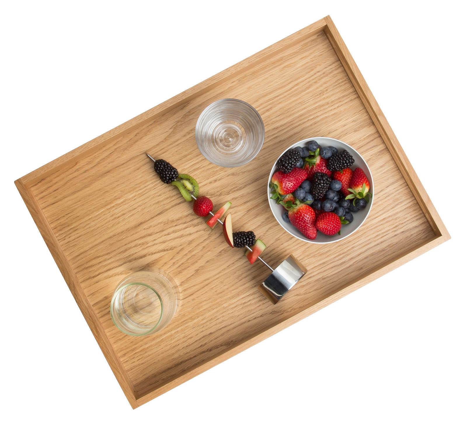Holztablett aus Eiche mit einer Schale voller Beeren, einem Glas Wasser und einem Fruchtspieß, aus der Vogelperspektive.