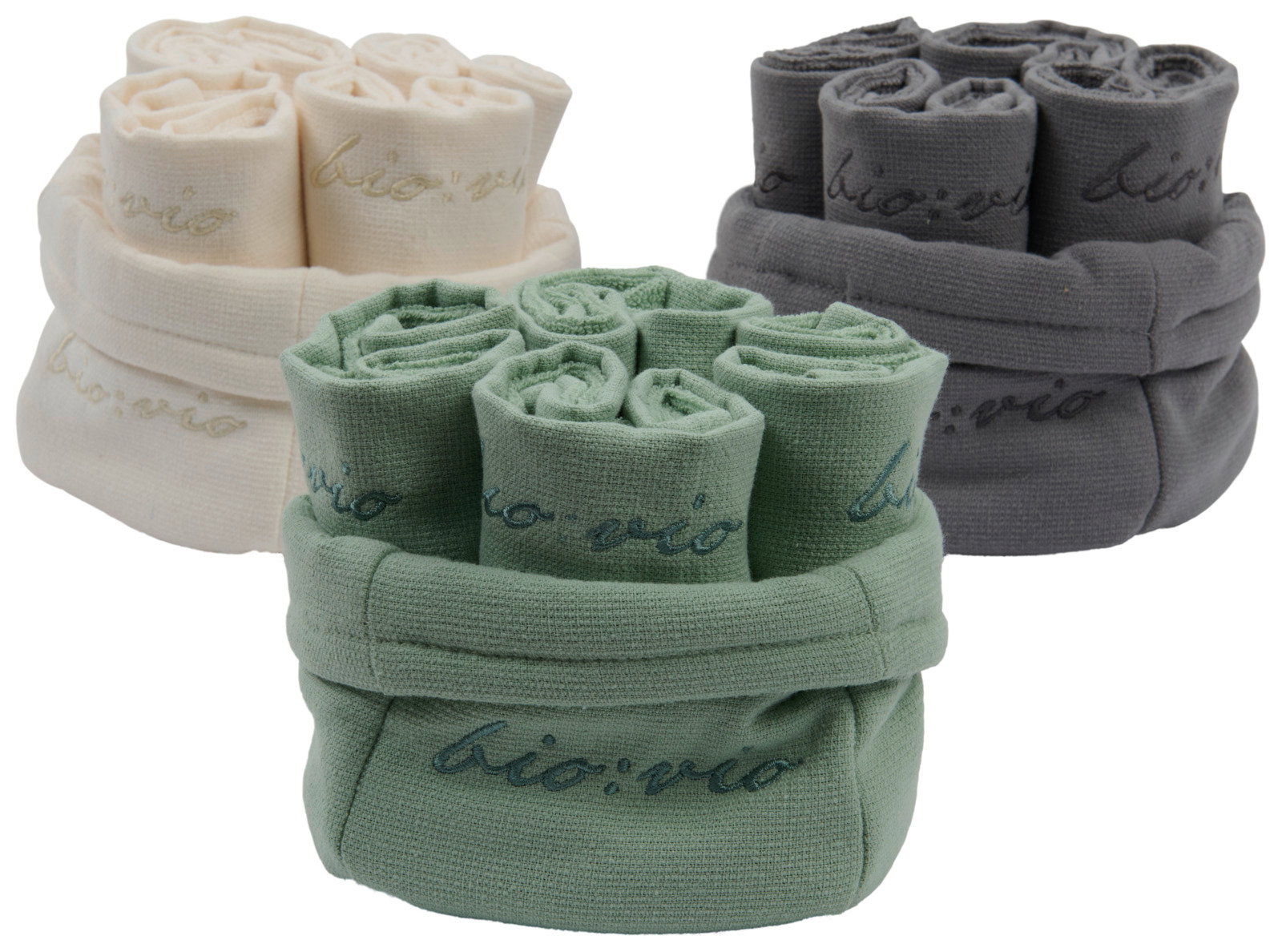 Drei Sets von Gästetüchern in den Farben Creme, Grün und Grau, aufgerollt und in Körben präsentiert, mit der Aufschrift 'bio:vio'. Perspektive von vorne.