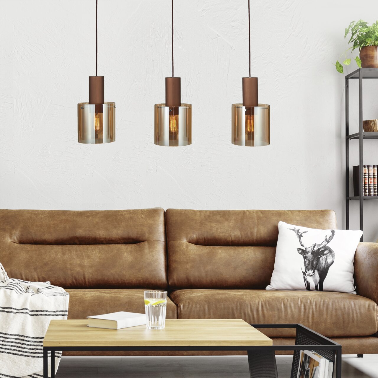 Drei moderne Pendelleuchten über einem braunen Ledersofa in einem stilvollen Wohnzimmer, seitliche Perspektive.