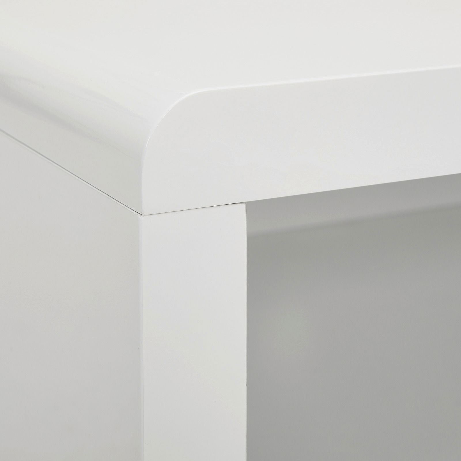 Nahaufnahme einer Ecke eines weißen TV-Lowboards mit abgerundeten Kanten, Perspektive von oben.